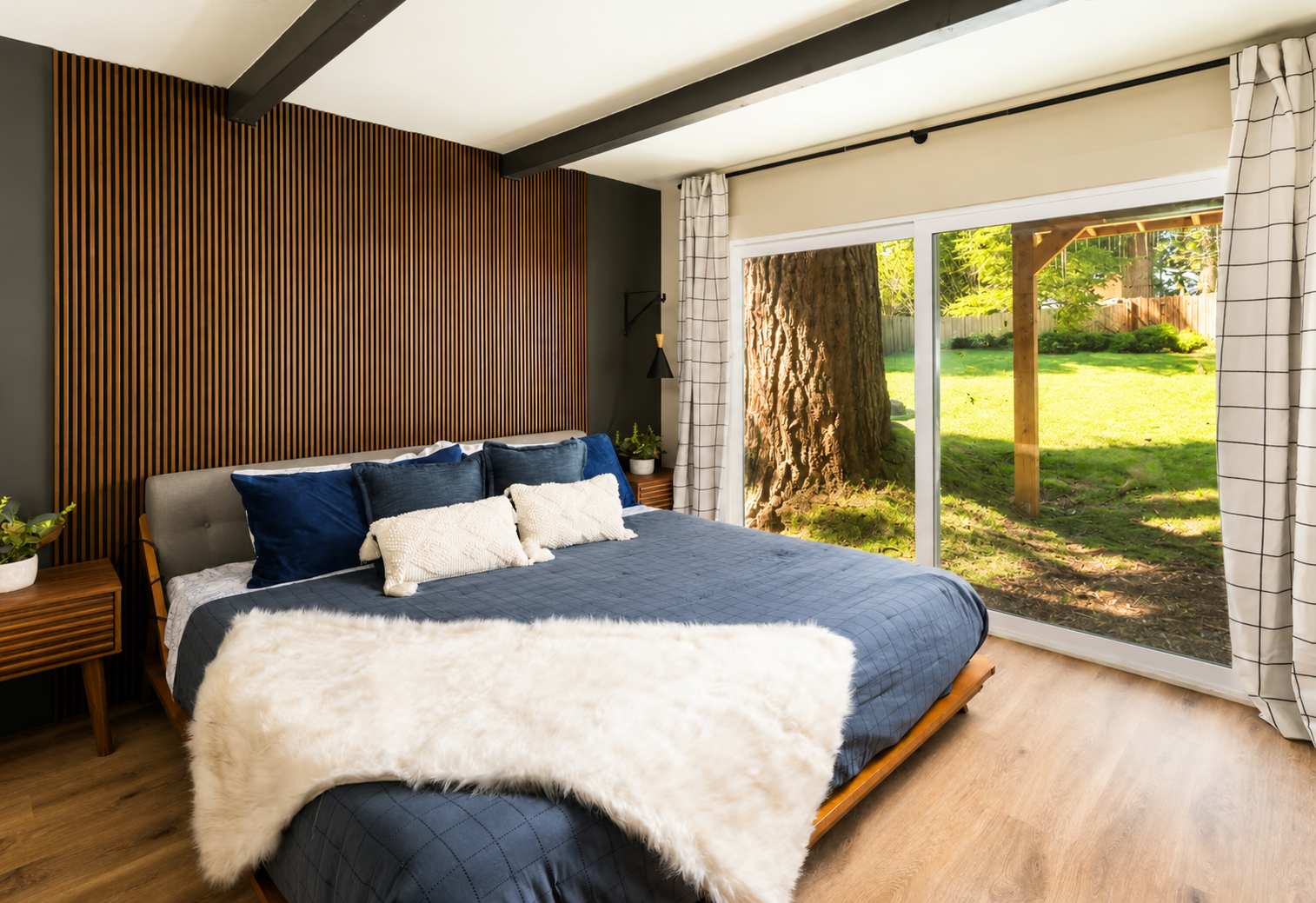 Bedroom in Kings Beach vacation rental with large window view of a tree and grassy yard. Cozy bed with blue linens.