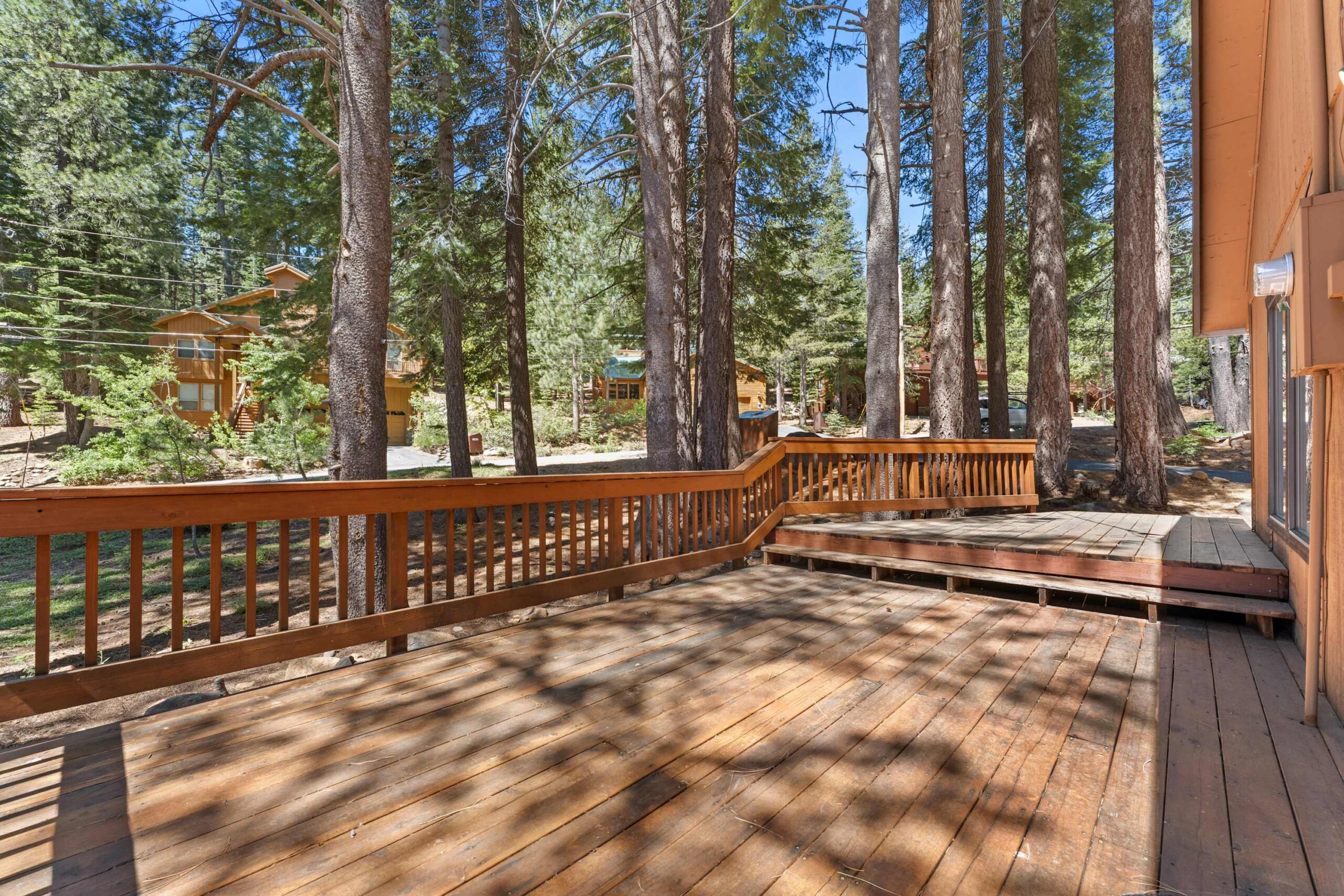 Wooden deck of a vacation rental in Truckee, surrounded by tall pine trees and neighboring cabins.