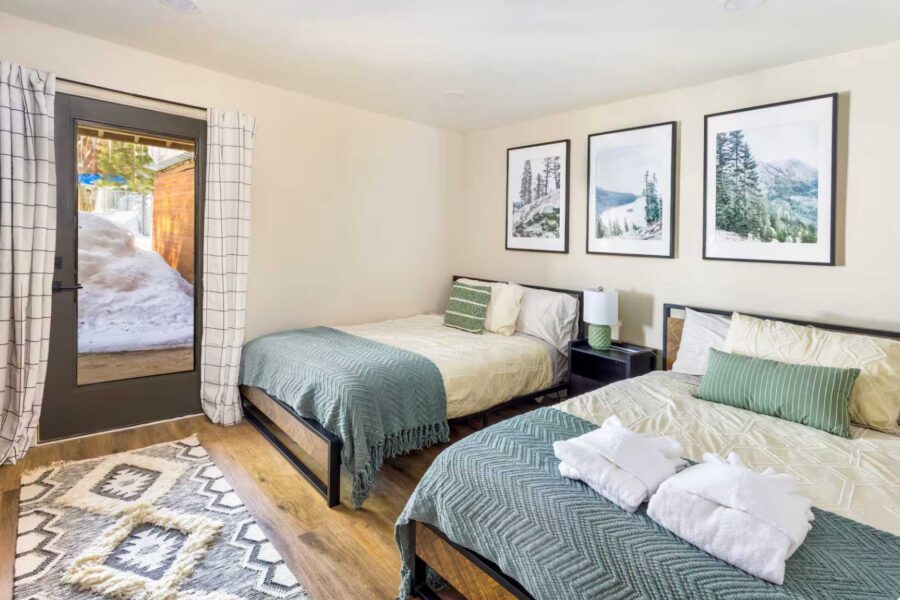 Two cozy beds in a Kings Beach vacation rental, decorated with nature art and a view of snow through the door.
