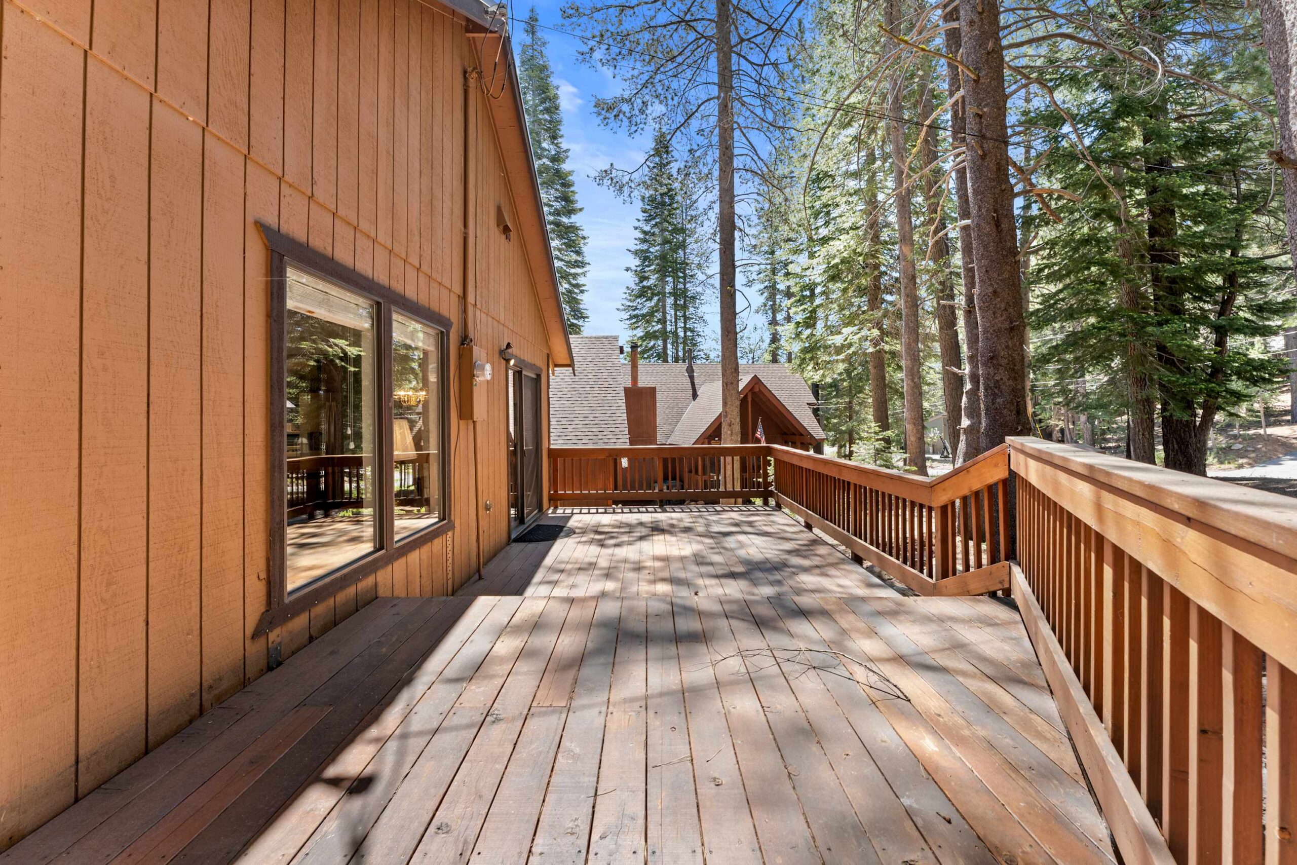 Spacious wooden deck of a Truckee vacation rental, surrounded by tall pine trees and neighboring rustic cabins.