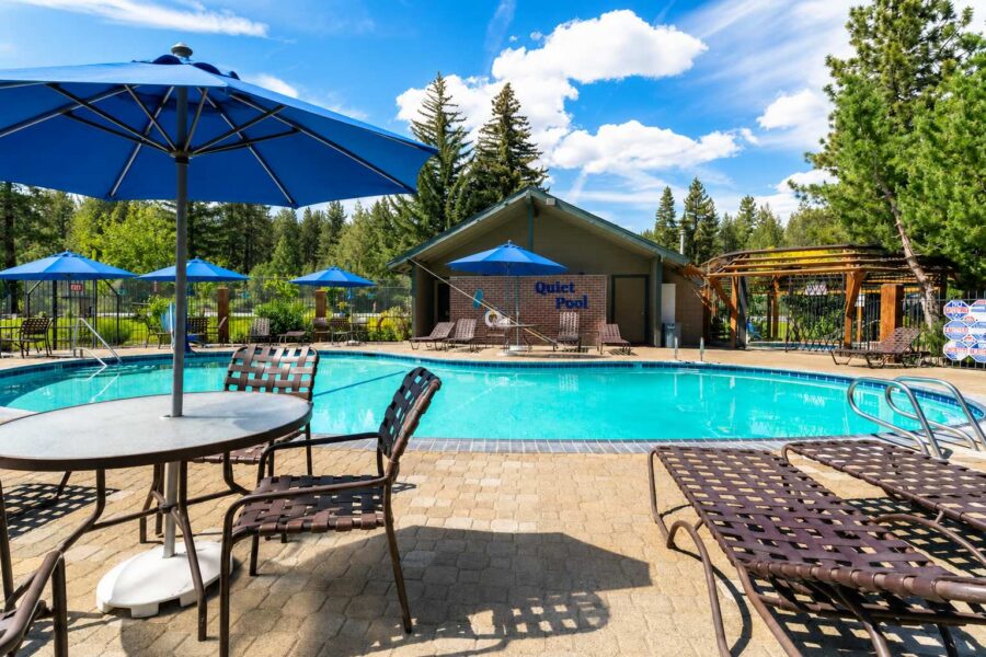 Outdoor pool area at a vacation rental in Tahoe City, featuring lounge chairs, blue umbrellas, and a serene forest backdrop.
