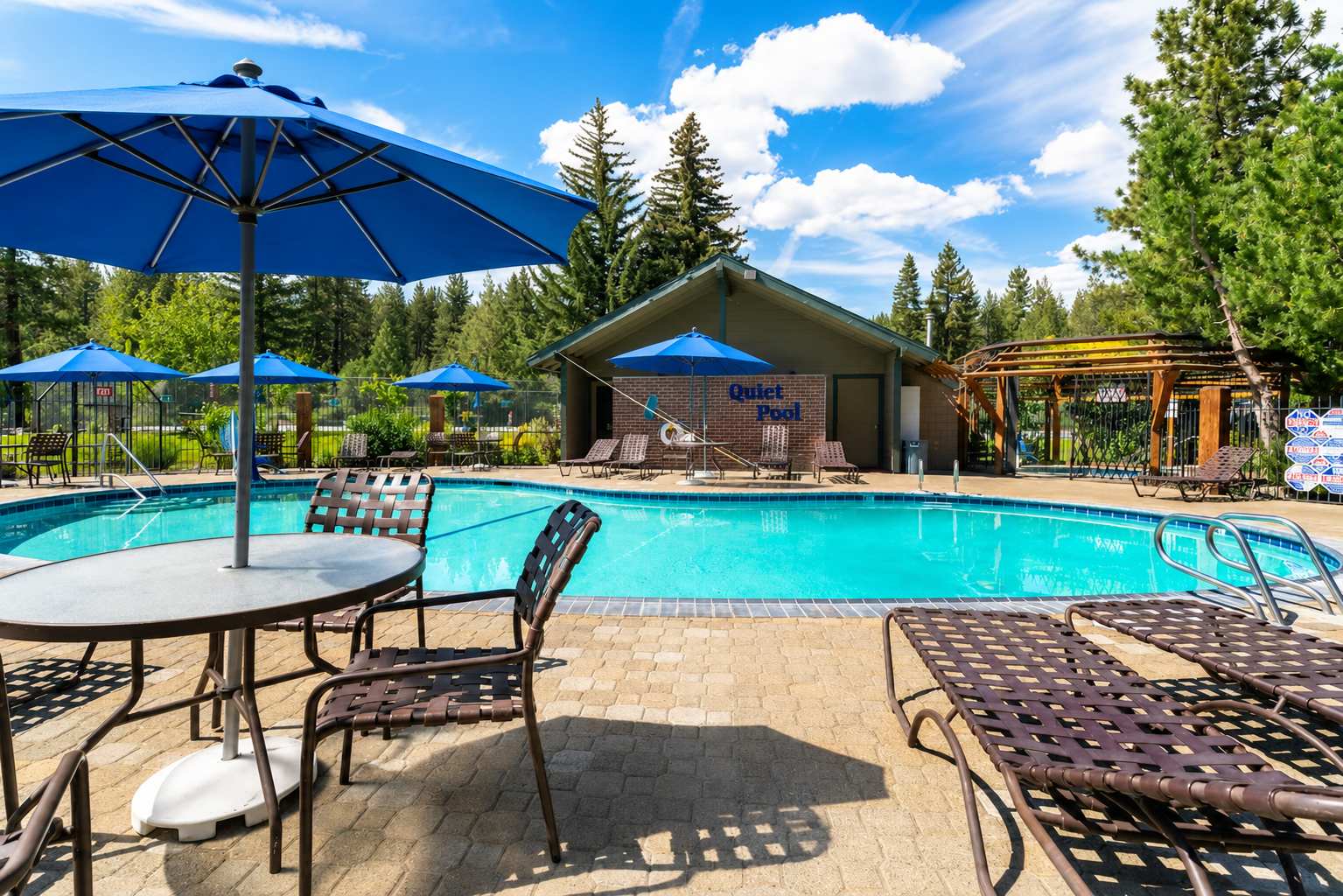 Outdoor pool area at a vacation rental in Tahoe City, featuring lounge chairs, blue umbrellas, and a serene forest backdrop.